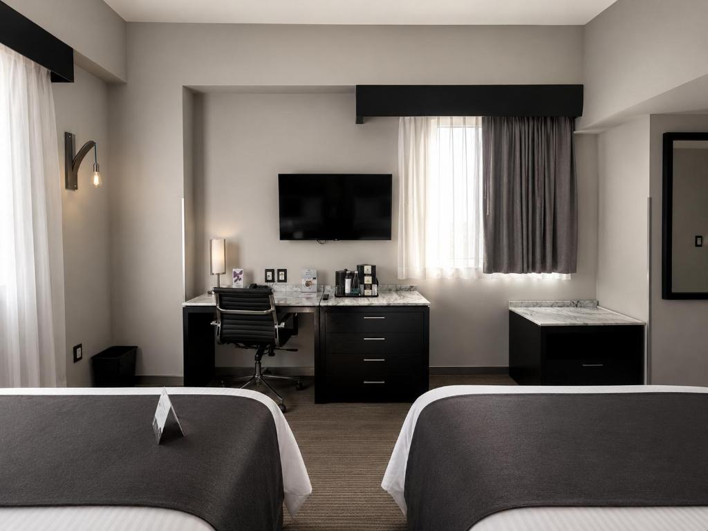 A two-bed room with a shared desk, TV, beverage station and curtained window.