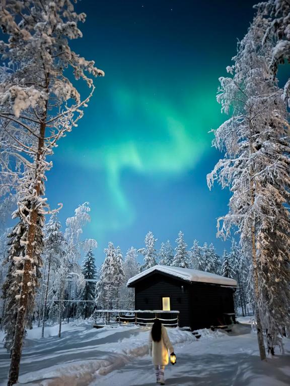 a woman walking in the snow in front of a cabin at Napapiirin Järvilomat in Rovaniemi