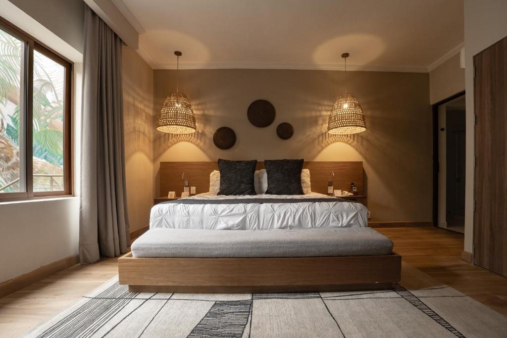 A warm bedroom features a large bed, woven pendant lights, and a leafy window.
