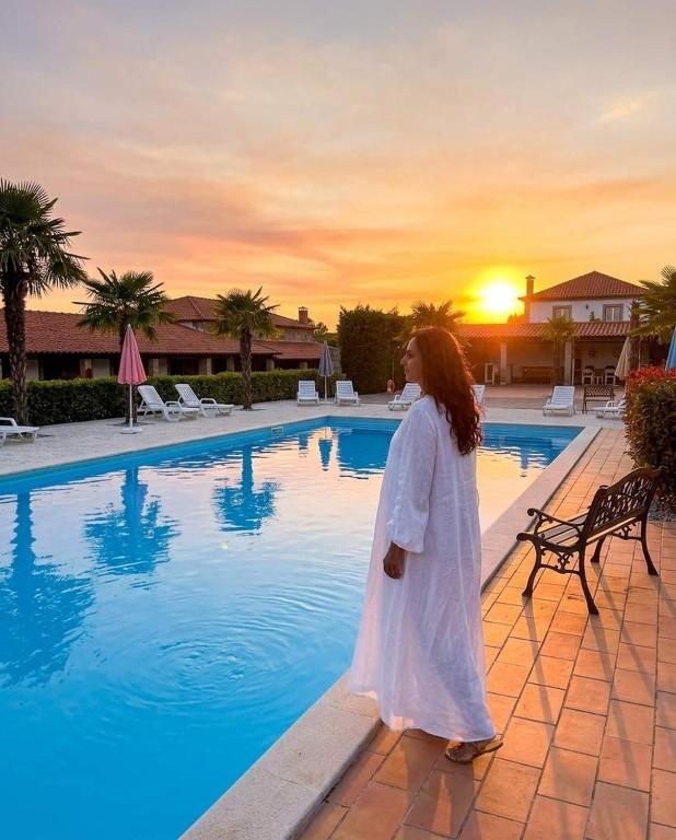 a woman in a white dress standing next to a swimming pool at Gojim Casa Rural in Armamar