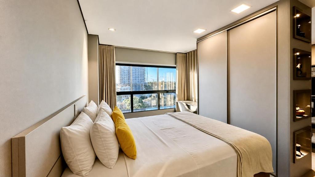 a bedroom with a bed with pillows and a window at Flat Elegante, Confortável e Com Uma Bela Vista in Campo Grande
