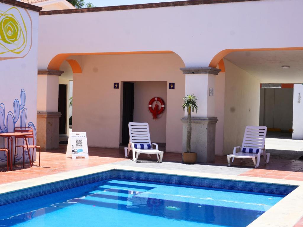 a swimming pool with two chairs and a table and a house at Hotel Buen Valle in Torreón