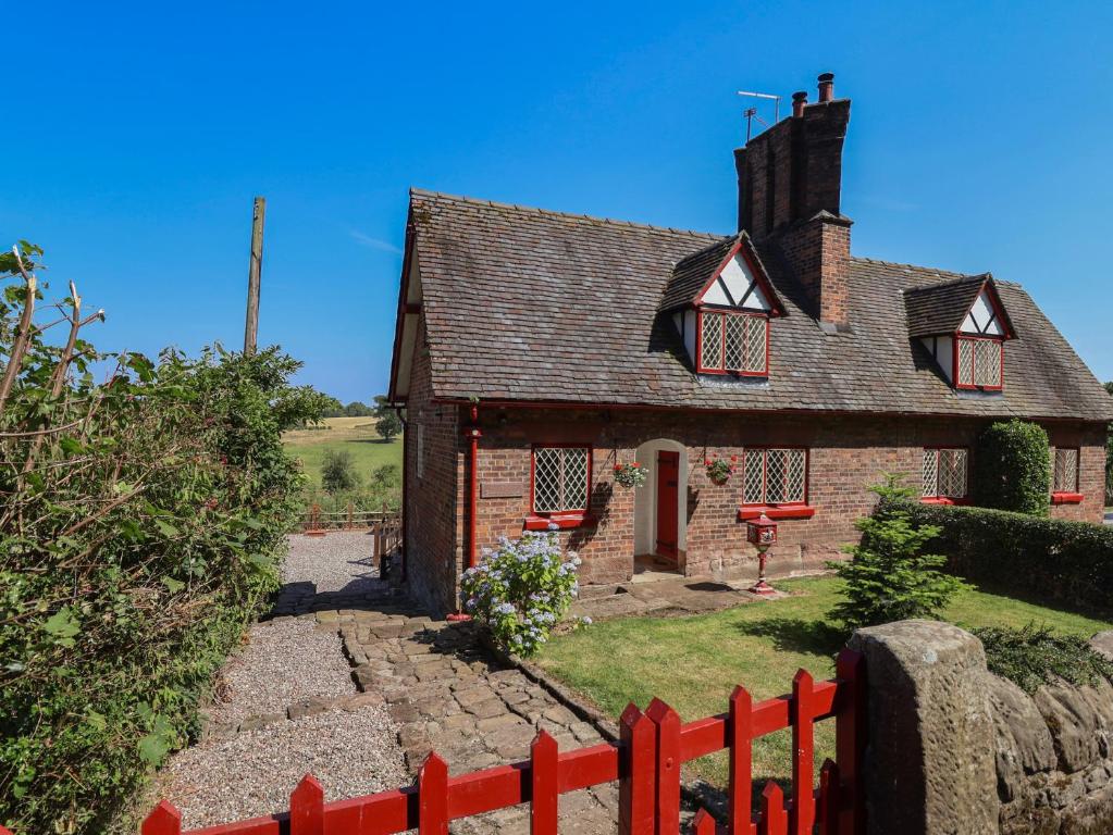 a small brick house with a red fence at 1 Fountain Cottages in Tarporley