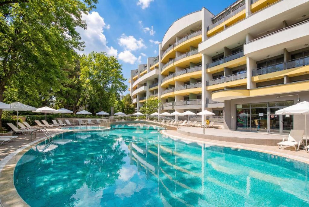 a swimming pool with chairs and umbrellas in front of a building at Hotel Perunika in Golden Sands
