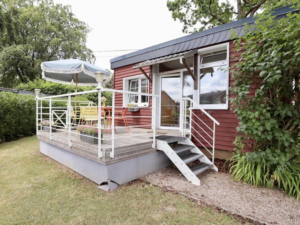 a red tiny house with a porch and a chair at Sous les Hetres in Robertville