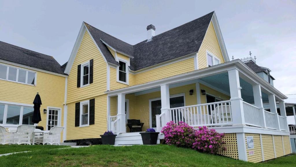 a yellow house with a white porch and flowers at Oceanfront Classic Maine Cottage In Close Walking Distance To Beaches! in York