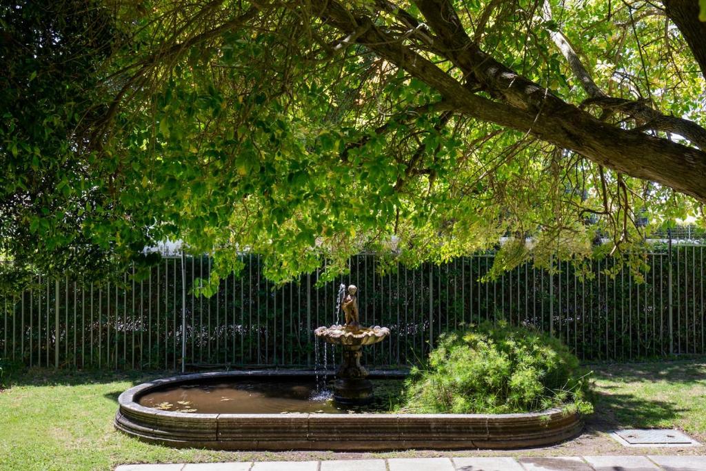 a fountain in front of a fence with a tree at Quiet Garden Flat Near Kenilworth Centre in Cape Town