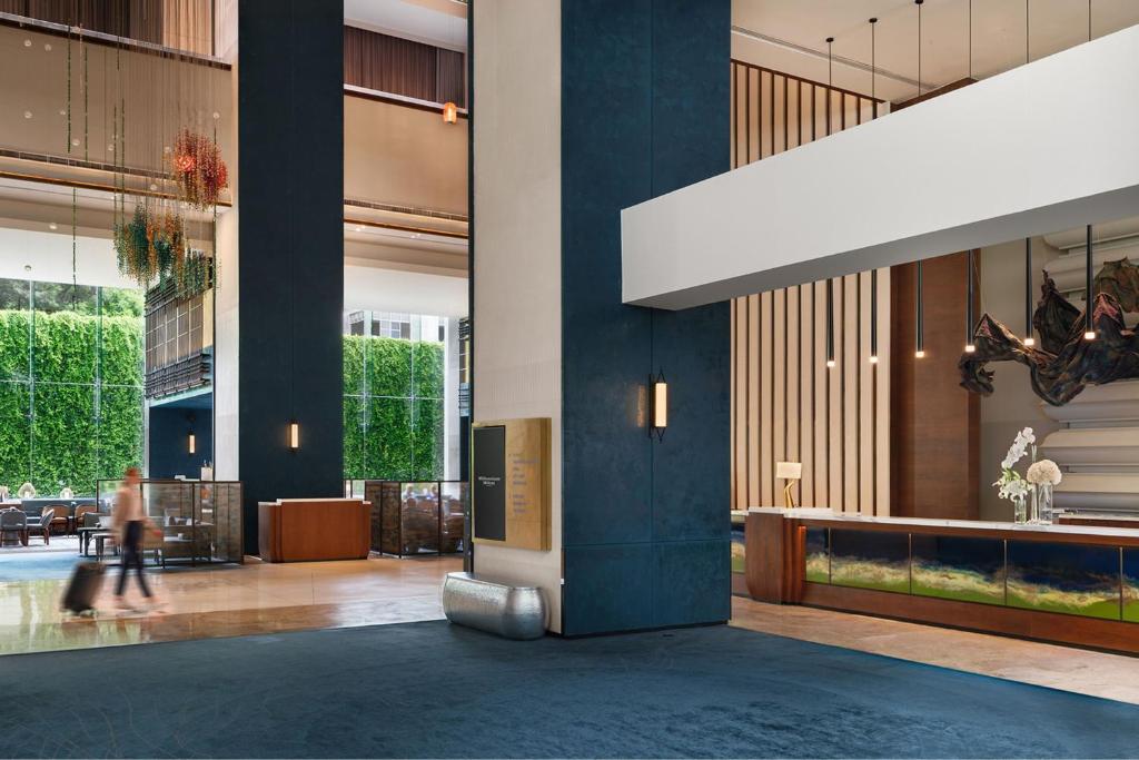 A tall contemporary lobby combines dark columns, greenery and a reception counter.