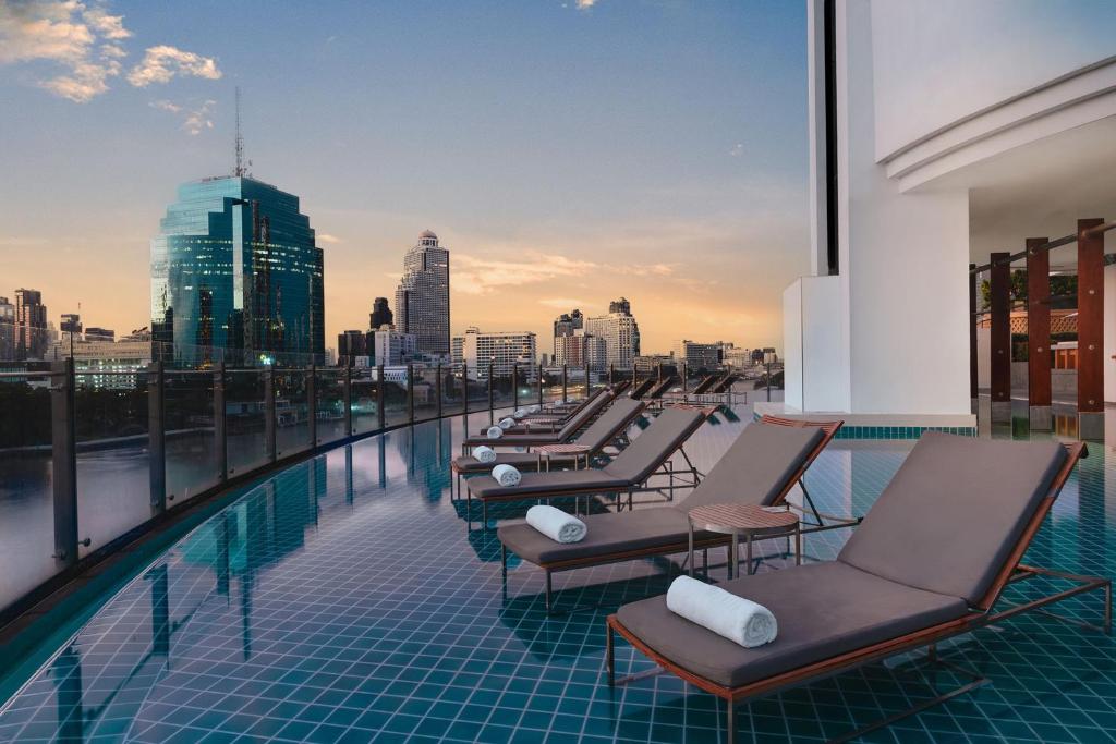 Pool loungers line a rooftop deck beside a Bangkok skyline.