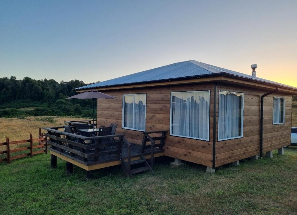 a wooden cabin with a deck and chairs in the grass at Cabañas Chiloé in Dalcahue