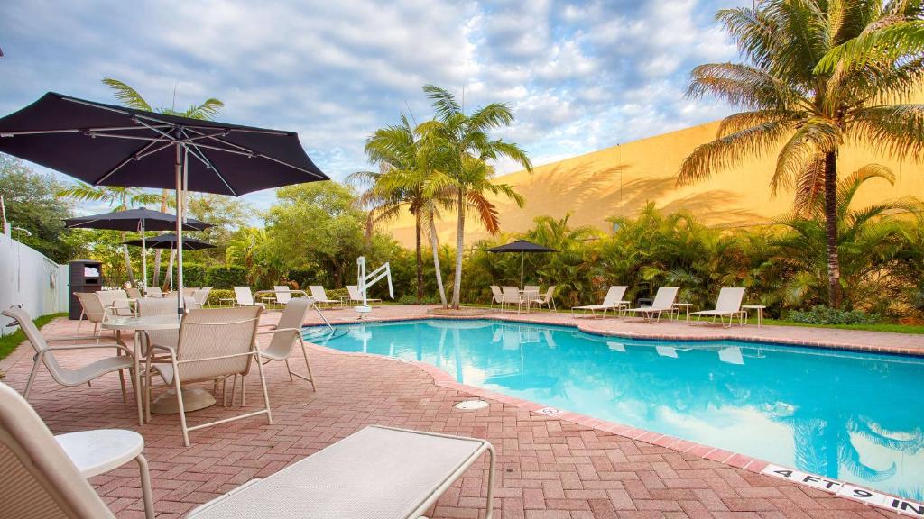 basen z krzesłami, stołami i parasolem w obiekcie Best Western Plus Miami-Doral/Dolphin Mall w Miami