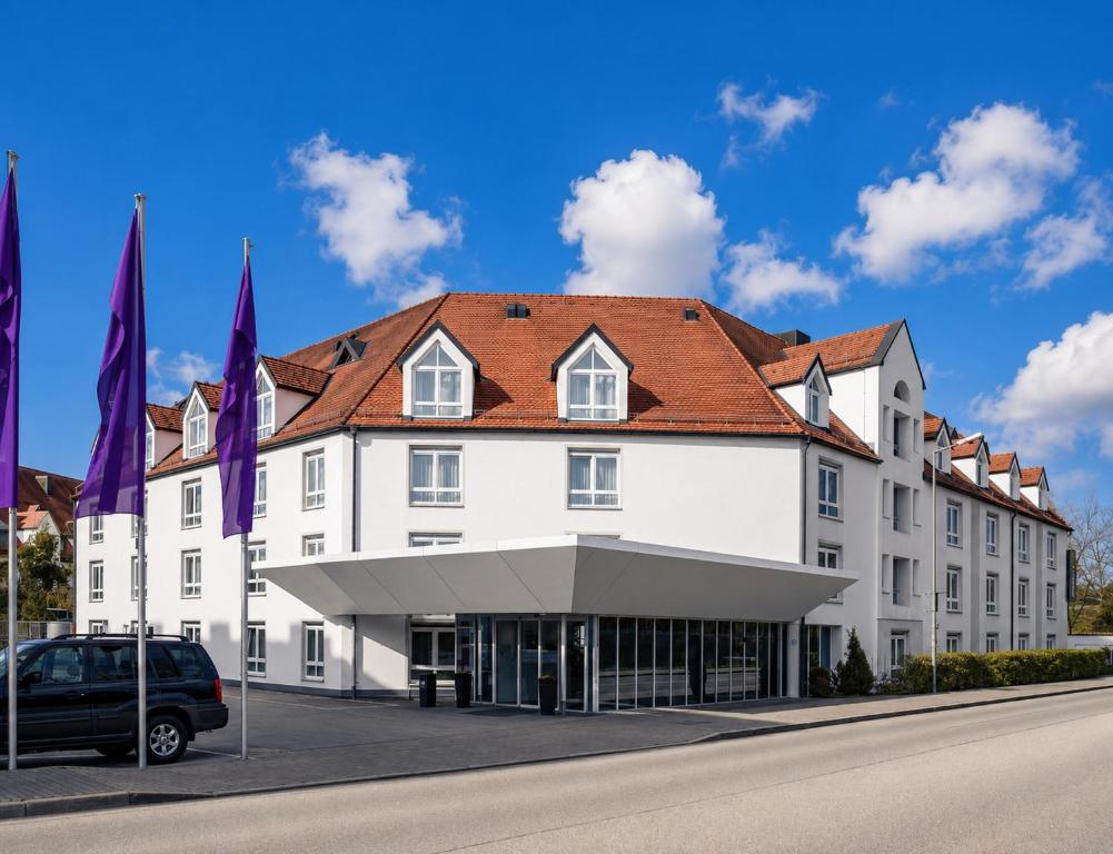 a large white building with a red roof at Sunday Hotel München Airport Freising in Freising