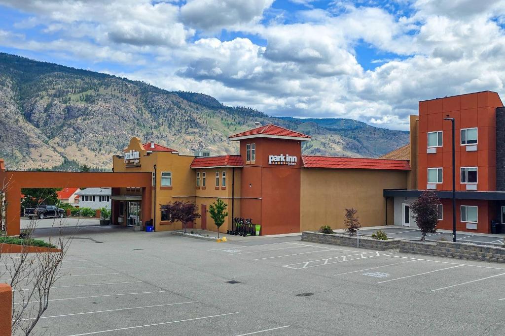 a hotel with a parking lot in front of a mountain at Park Inn by Radisson Osoyoos in Osoyoos