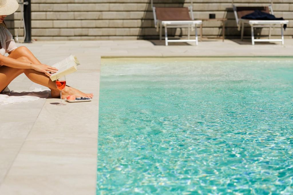 a woman reading a book next to a swimming pool at Appartamento Maison Sabrina con vista giardino in Borgofranco dʼIvrea