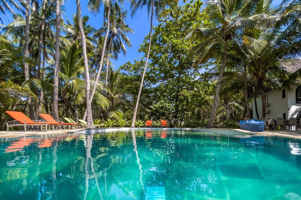 a swimming pool with palm trees in the background at Watano Beach House Diani in Diani Beach