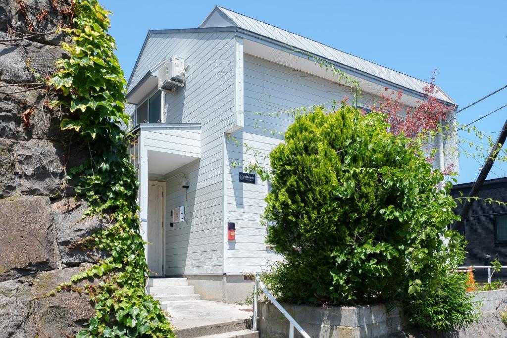 a white house with a tree in front of it at plus81 OTARU Entire House 9min Walk from Minami Otaru Station in Otaru