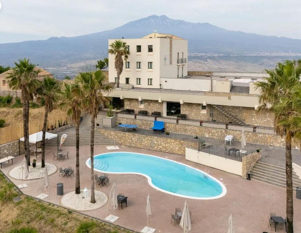 a swimming pool in front of a building with palm trees at Kento Resort Hotel in Centuripe