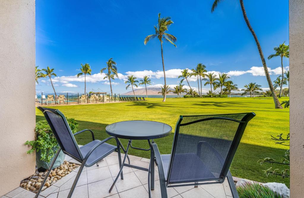 a patio with a table and chairs and palm trees at KIHEI SURFSIDE #109 in Wailea