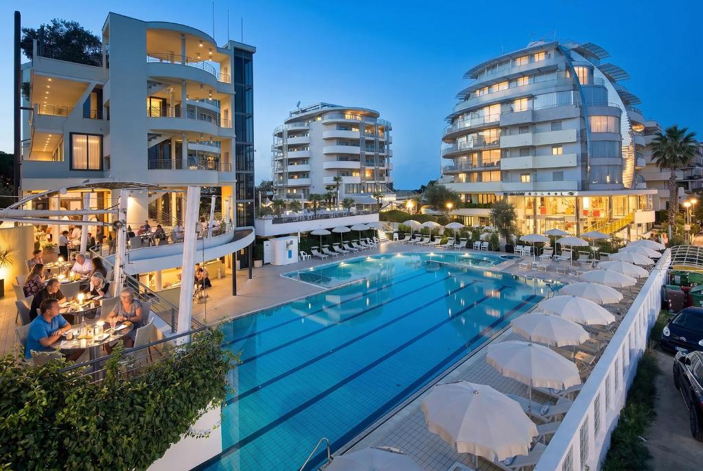 a swimming pool with white umbrellas next to buildings at Hotel Premier & Suites - Premier Resort in Milano Marittima