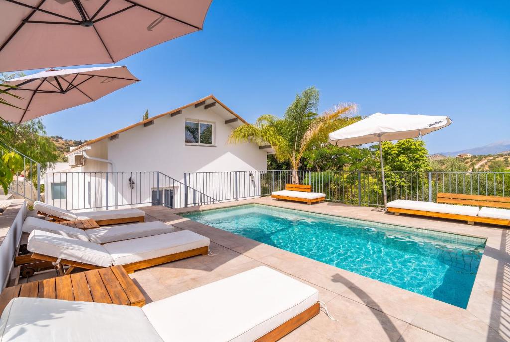 a pool with chairs and umbrellas next to a house at Cubo's Violeta Rural House in Coín