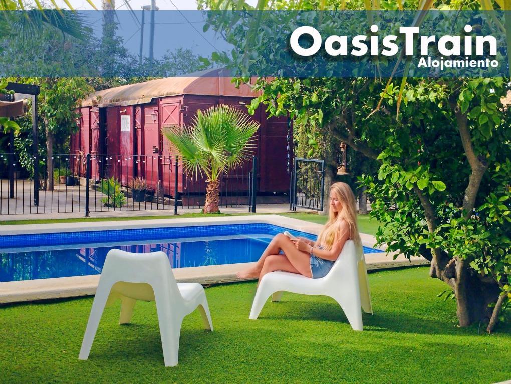 a woman sitting in a chair next to a pool at OasisTrain 03 - Alojamiento Vagón Rural in Murcia