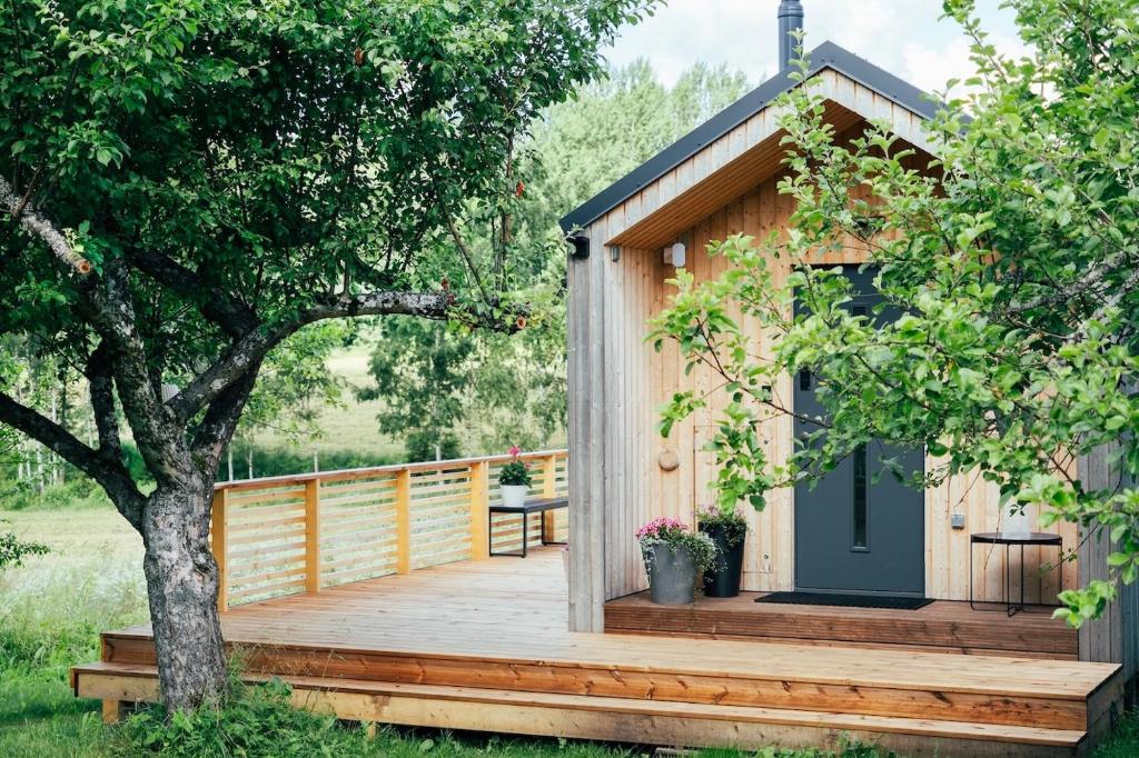 a wooden cabin with a deck and a tree at Suur Muna Apple Garden Tiny Houses in Haanja