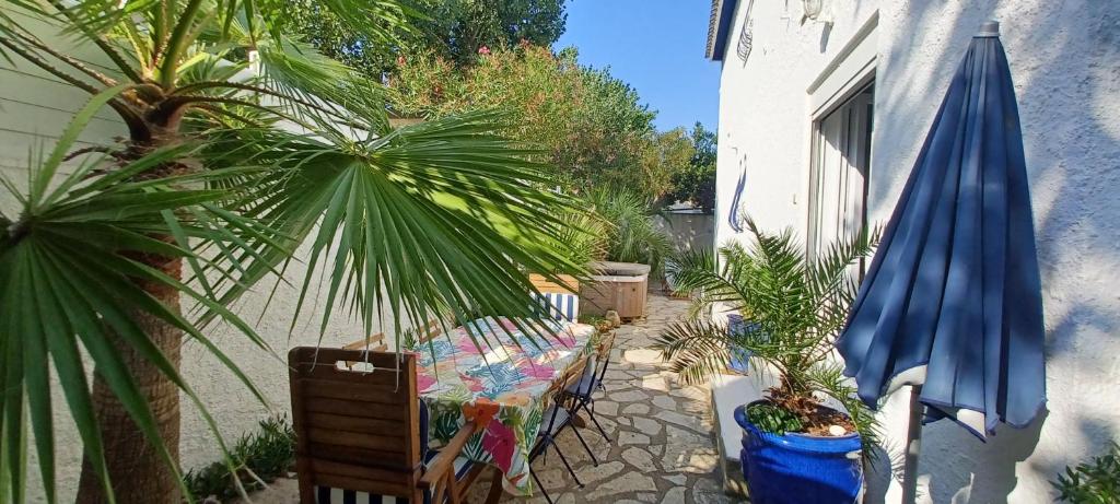 a patio with a table and an umbrella and palm trees at Appartement Jardin et Spa in Valras-Plage