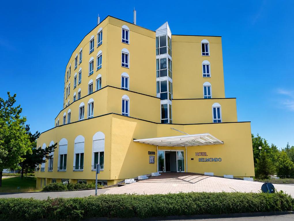 a yellow building with a blue sky in the background at Hotel Belmondo Leipzig Airport by Mayburgh in Wiedemar