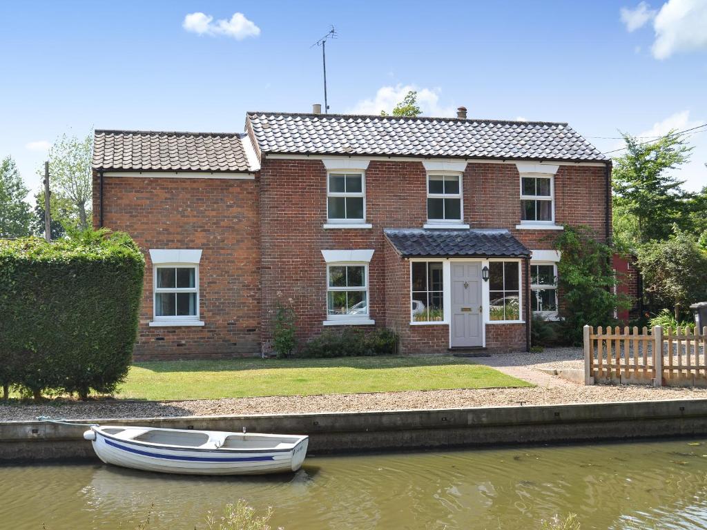 a red brick house with a boat in the water at Riverside - Ukc2296 in Stalham