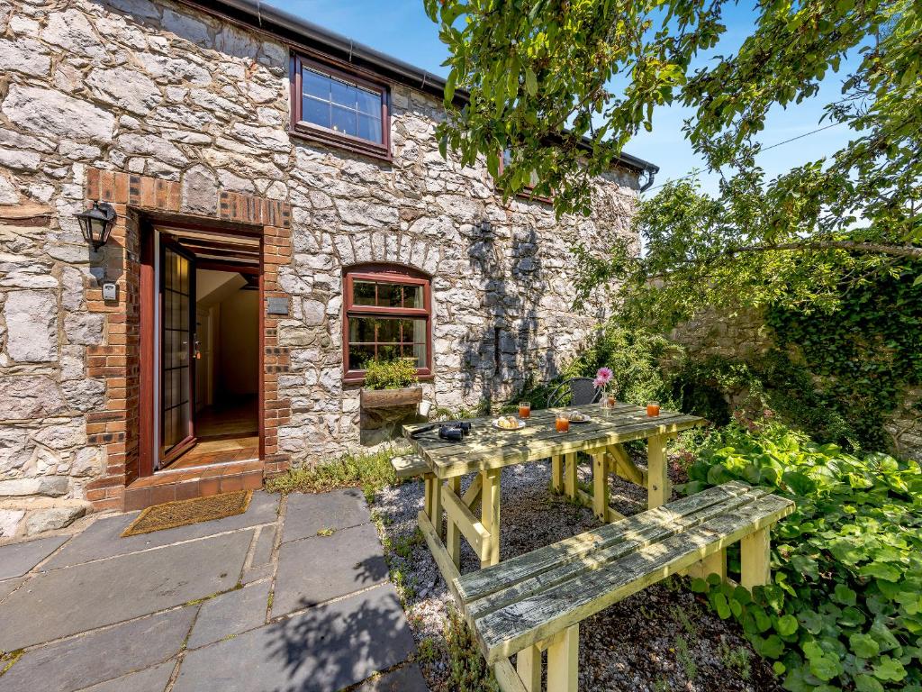 a stone house with a wooden table in front of it at Primrose Cottage - Ukc6679 in Bettws-yn-Rhôs
