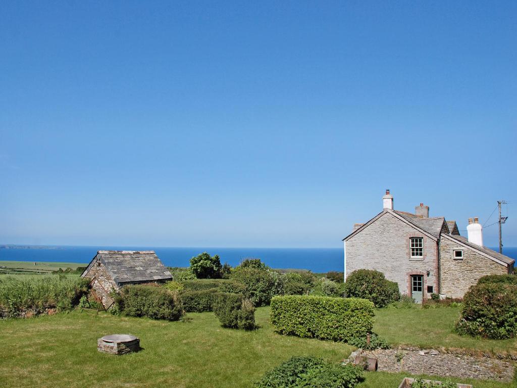 an old stone house with a lighthouse on the coast at Downhouse in Delabole