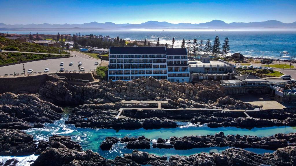 a building on the beach with rocks and water at The Point Hotel & Spa in Mossel Bay