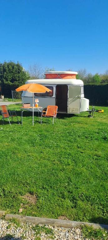 a rv parked in a field with a table and an umbrella at Chez Flo&Fred Caravane Vintage in Barbery
