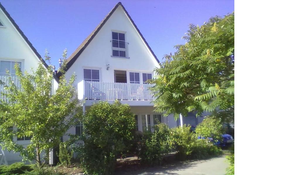 a white house with a balcony and trees at Ruhige, moderne Maisonette Ferienwohnung Rügensonne mit großem Balkon - umgeben vom Wasser in Breege