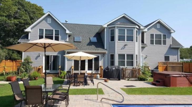 a house with a patio with chairs and umbrellas at Beautiful 6-Bedroom Escape Featuring a Private Pool in Hampton Bays