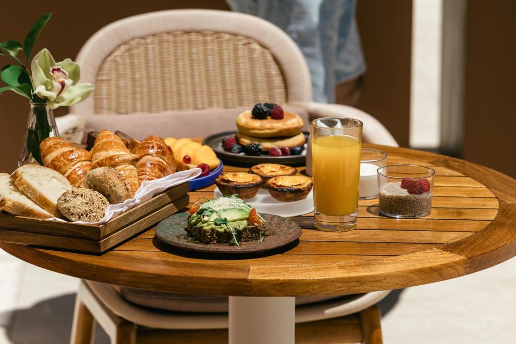 A round wooden table set with pastries, bread, fruit, juice, and plated breakfast dishes.