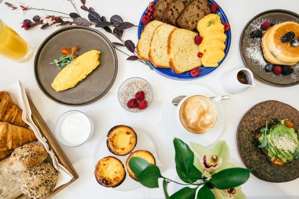 An overhead breakfast table filled with breads, pastries, fruit, coffee, and savory plates.