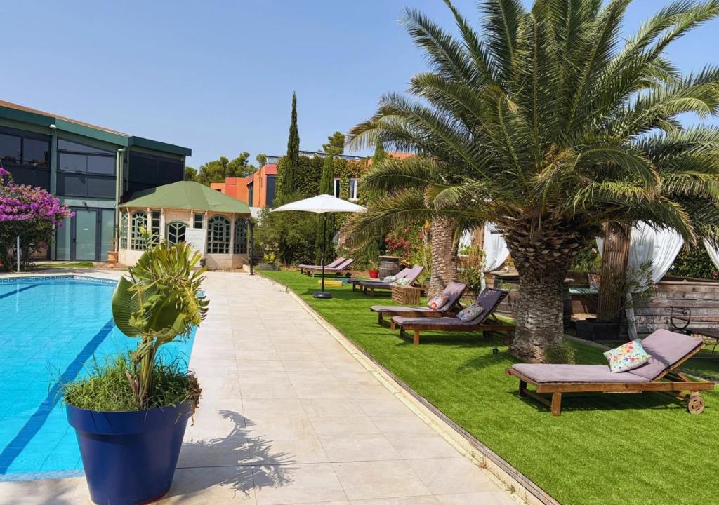 a resort with a pool and palm trees and benches at Tropic Hôtel in Rivesaltes