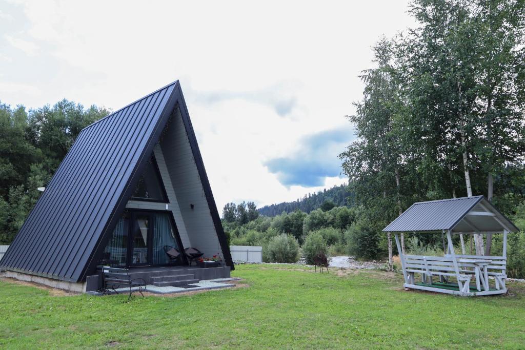 a black roofed house with a gazebo in a field at A-frame cottage in Mykulychyn
