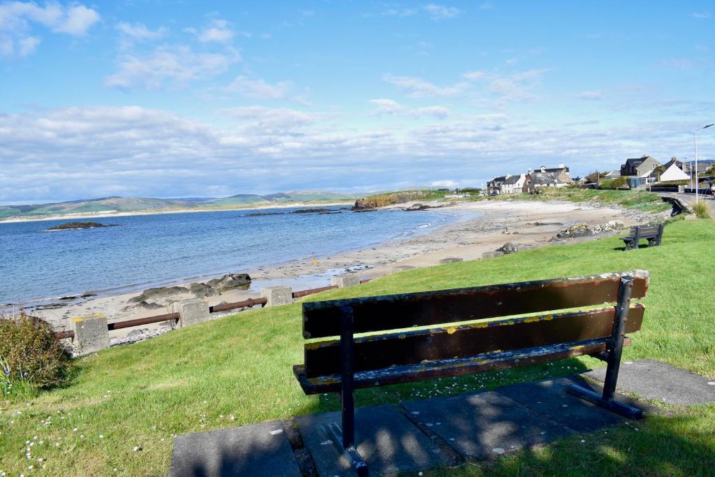 a bench sitting on the grass next to a beach at Spacious home in Machrihanish in Machrihanish