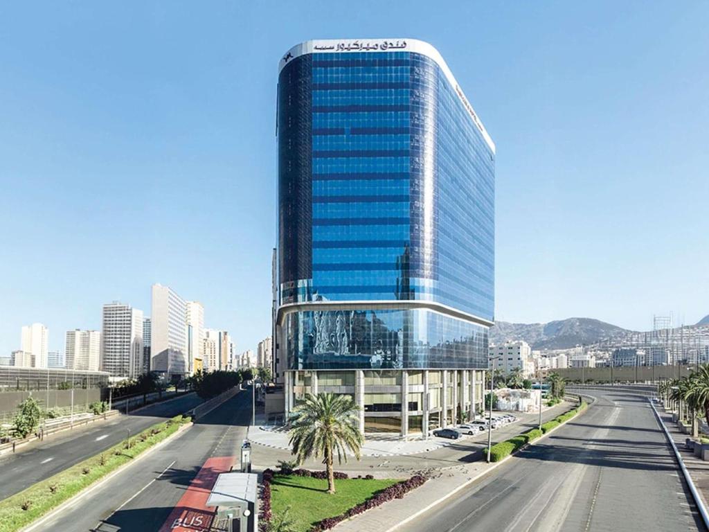 a tall glass building in the middle of a street at Mercure Makkah Aziziah in Mecca