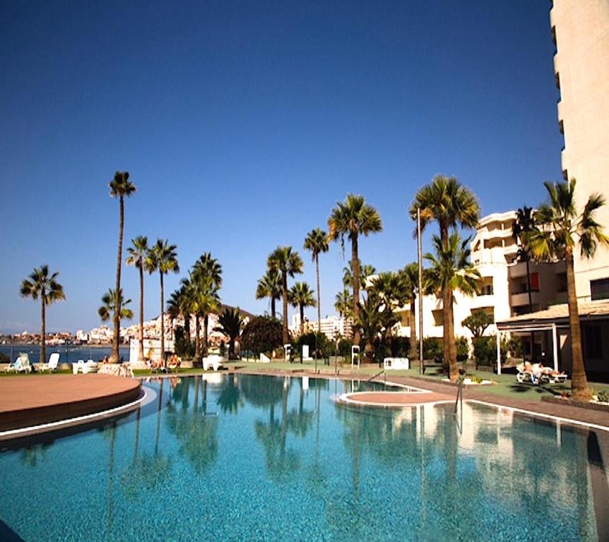 a large swimming pool with palm trees and a building at Amazing sea view in Los Cristianos in Los Cristianos