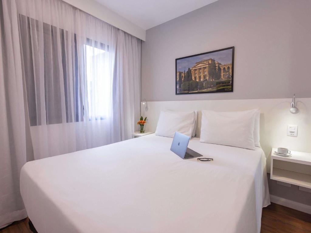 a bedroom with a white bed with a laptop on it at Mercure São Paulo Berrini in São Paulo