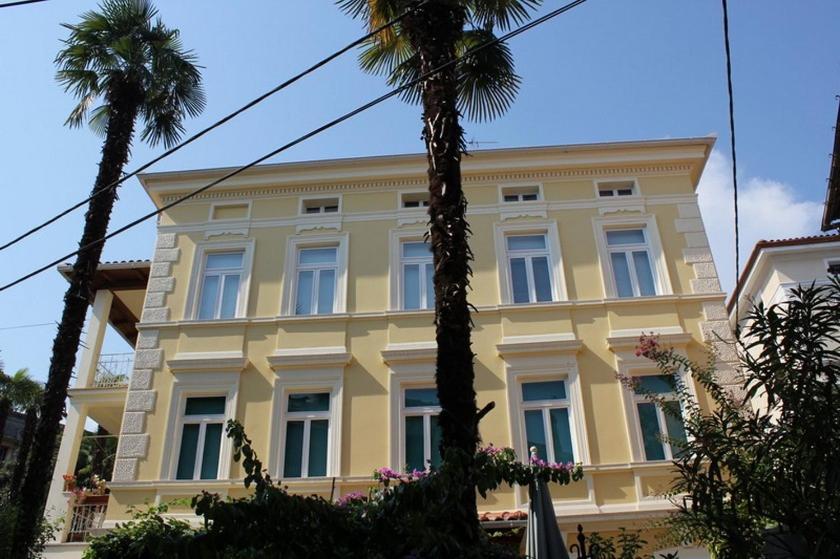 un grand bâtiment jaune avec des palmiers devant lui dans l'établissement Rooms Alida, à Opatija