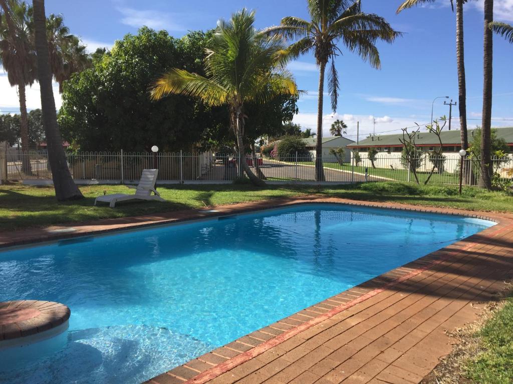 a swimming pool with palm trees in a yard at Carnarvon Gateway Motel in Carnarvon