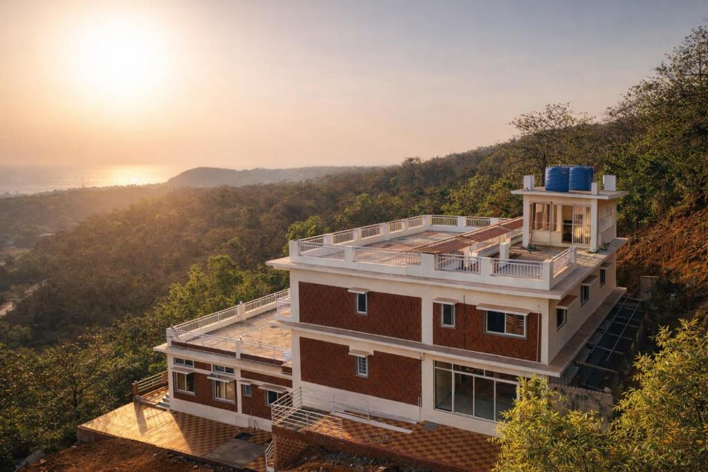 a house on a hill with the sun in the background at Anandi Hotel Guhagar in Guhagar