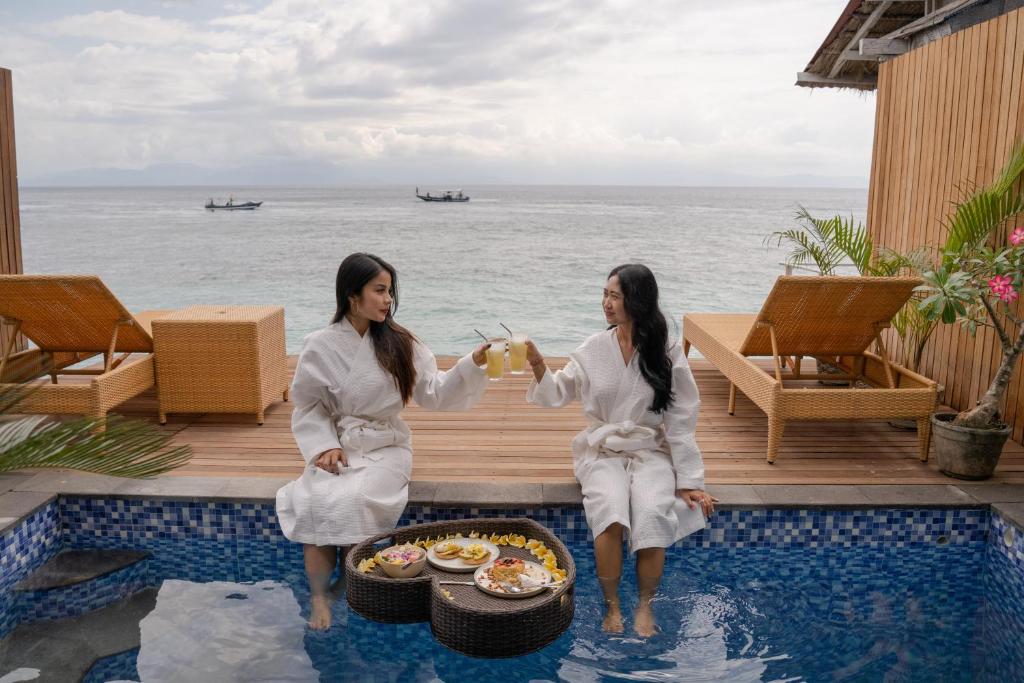 two women in white robes sitting next to a pool at Sunrise Cottage in Nusa Penida