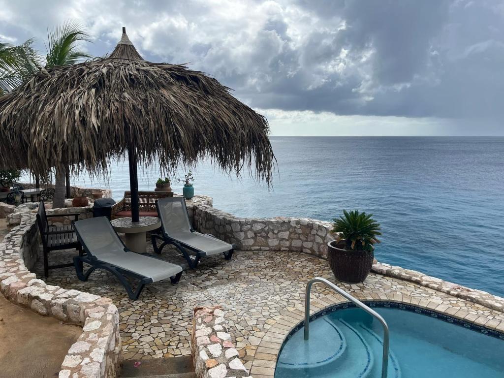 a swimming pool with chairs and an umbrella and the ocean at Lagun Paradise Curacao in Willemstad