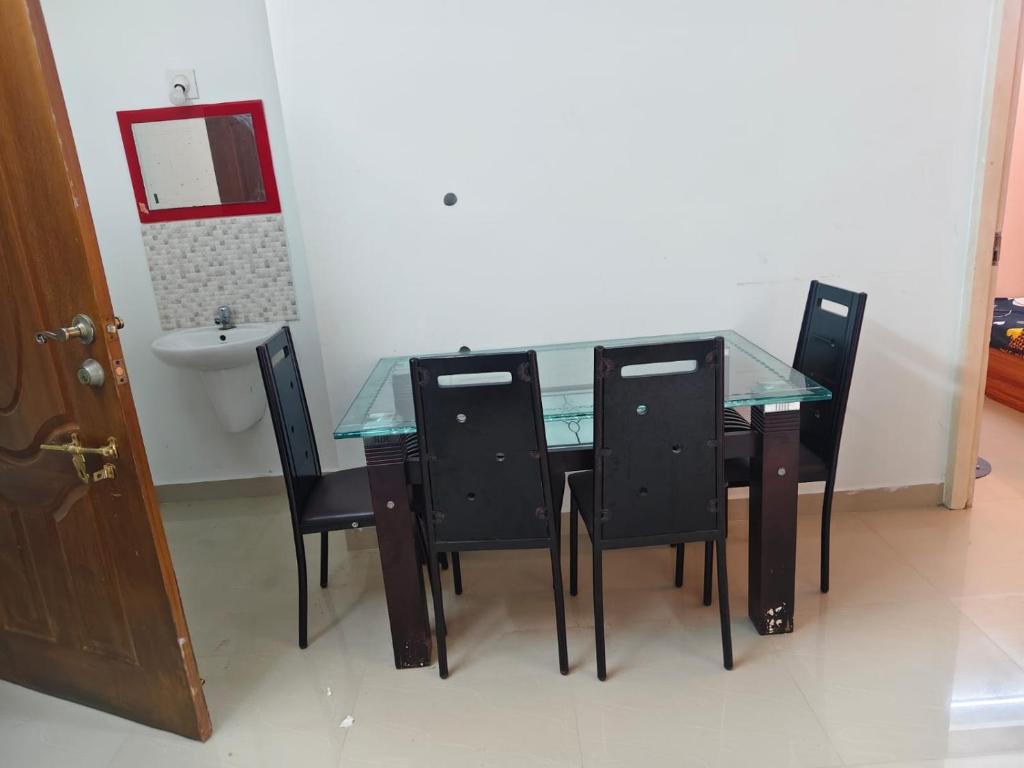 a glass table and four black chairs in a room at Sheelas stay in Guruvāyūr