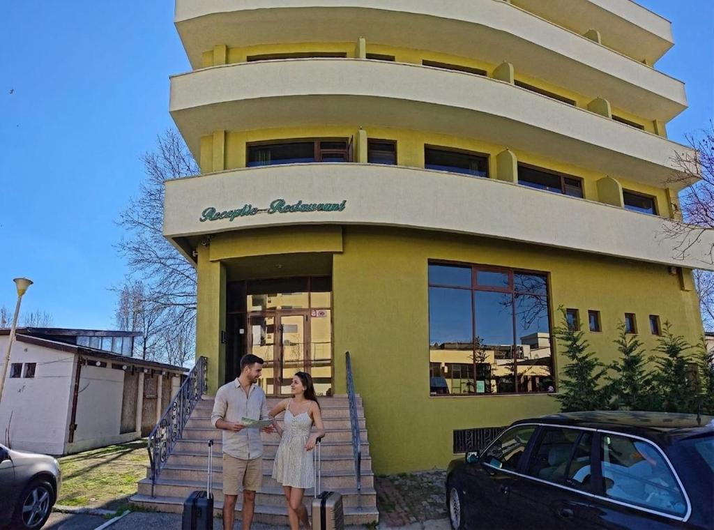 a man and a woman standing in front of a yellow building at Alma by iVAVev in Mamaia